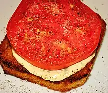 An open-faced tomato sandwich seasoned with salt and pepper atop the tomato