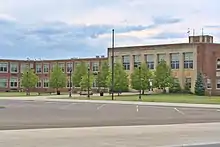 Photograph of a high school with blue sky above and parking lot in foreground