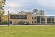 Photograph of a sandstone colored, modernist brick school building with tall black windows