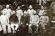 Outdoor photo of nine men, five seated and four standing