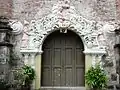 Ornate side portal, featuring pink reliefs of the Visitation at the top, and figures of Saint Zachary (vested as a kohen) and Saint Elizabeth to the sides