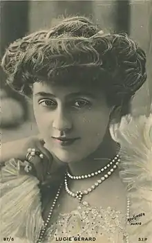 A closeup handcolored photograph of a white woman with her wavy hair in a bouffant updo, wearing pearls and light-colored lace