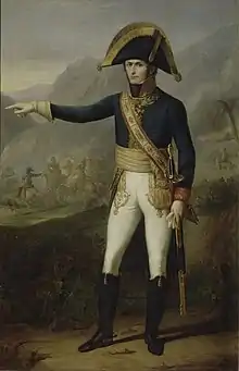 Painting of a standing man in a dark blue military uniform with white breeches and black boots. The stern-looking man, who wears a large black bicorne hat with gold edging, points to the observer's left.