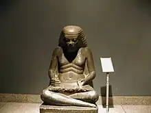 Seated scribe with part of scribe equipment on shoulders(2-basin mixing palette over left shoulder)