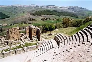 A large stone staircase in the foreground leads down to a ruined building, overlooking a panoramic view of several mountains and valleys.