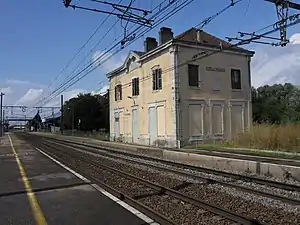 Double-tracked railway line with side platforms and disused two-story building with hipped roof