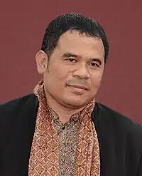 Garin Nugroho in a casual black-and-red shirt, mildly smiling, with a red background.