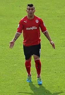 A footballer wearing a red jersey with black shorts