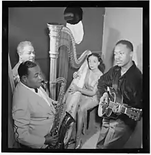 Four Black musicians in a small booth, three men and one woman (the harpist).