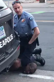Police officer Derek Chauvin stares into the camera as he kneels on the neck of George Floyd, who is lying on his stomach on the street