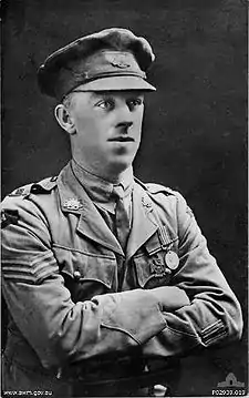 A head and shoulders portrait of a man in military uniform. His arms are crossed.
