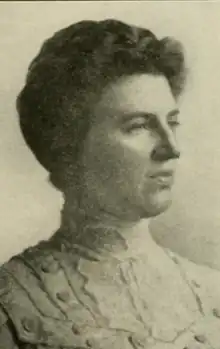 A white woman with dark hair dressed back to the nape, wearing a lacy high-collared shirtwaist or dress