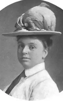 A young white woman wearing a collared shirt, a necktie, and a large brimmed hat.