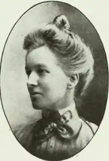 A white woman with fair hair dressed in a bouffant updo, wearing a high-collared striped blouse or dress, in an oval frame