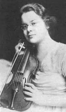 A young white woman wearing glasses, holding a violin.