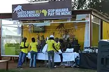 Glass house with brown sign and four people in yellow T-shirts in front