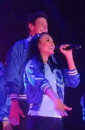 A man and woman in blue letterman jackets singing.