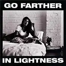 A black-and-white image featuring a woman and a dog sitting on a bed. A black border surrounds this image. White bold text on the top and bottom of the image reads "Go Farther in Lightness"