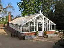 A greenhouse, the bottom section is brick and the top half is a white wooden frame with glass panels.