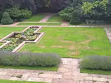 a stone-edged cruciform pond on the left, on the right is a lawn with patterns formed by parched grass.