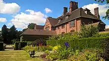 a grass lawn and a border of flowering plants in front of a large redbrick house.