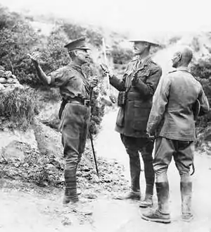 three men dressed in uniform standing on scrubby terrain, in conversation