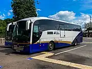 A white, blue and gold coach parked in a bus station.