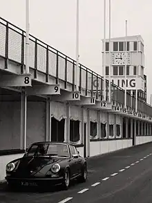 Black and white picture showing dark colours car in a pits area.