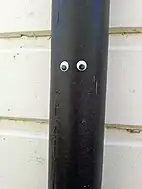 A pair of small googly eyes attached to a black drainpipe against the wall of a building