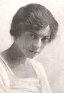 A young white woman with wavy dark hair, wearing a light-colored top with a square neckline