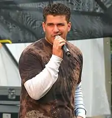 A man with dark curly hair singing into a microphone