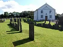 Gravestones in grassed-over graveyard with white-painted chapel in the background