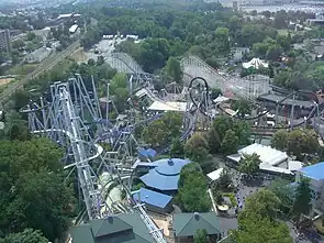 An overhead view of the Great Bear roller coaster among several attractions. The Great Bear roller coaster is left and center of the image, with steel roller coaster SooperDooperLooper located in the middle and left. The Coal Cracker log flume is on the left under the tracks of the Great Bear. The Comet wooden roller coaster is seen in the background, with various paths, buildings, and trees surrounding each attraction.