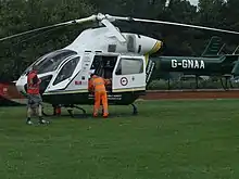 The former helicoper of GNAAS, G-GNAA, shown landed in a field in Darlington. A man in hi-vis clothing is leaning in its opened side door.