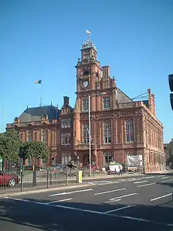 Large "gothic" red brick civic building with clock tower and road to the front