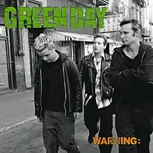 A black-and-white photo of all the band's members walking on sidewalk with the city in the background. We see the band's name written in green, and the album's title written in yellow.