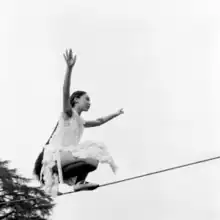 Black and white image of woman with dark hair balancing on a tightrope with her arms raised