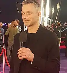 Grzegorz Damięcki wearing a suit, holding a microphone, at the premiere of the film Podatek od miłości in 2018