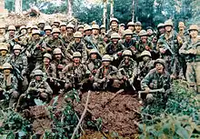 Men in military camouflage, wearing helmets, carrying long guns, and shouting