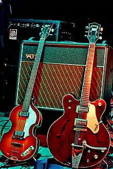 Two electric guitars, a light brown violin-shaped bass and a darker brown guitar resting against a Vox amplifier