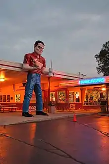 Gus's Giant Muffler Man, in front of a restaurant, with neons lit, dusk