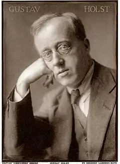Bespectacled white man of middle age, clean-shaven, leaning on his right hand and looking at camera