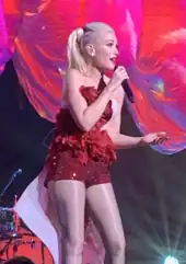 A color photograph of singer Gwen Stefani, performing live in a sparkly red outfit.