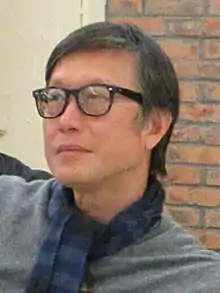 Lau wearing a gray shirt and a blue striped scarf