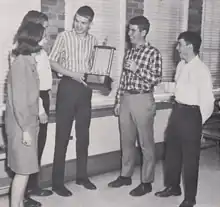 Photograph of high school debaters standing with a trophy