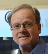 tight headhsot of an older man with cglassed against a colored background