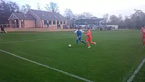 Hallam (in blue) on the attack in an NCEL match against Louth Town in 2014. The new clubhouse and main stand are in the background