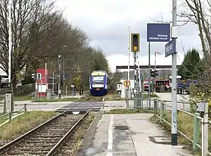 Purple-and-white train stopped at platform just before a level crossing