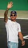 Lewis Hamilton wearing a black baseball cap and white T-shirt and is waving to the crowd