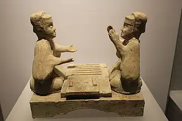 Han dynasty glazed pottery tomb figurines playing liubo, with six sticks laid out to the side of the game board